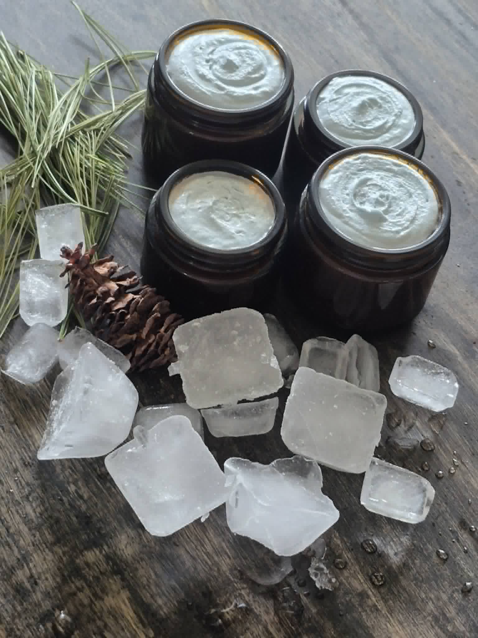 Jars of pale blue whipped Glacier Vista Tallow Balm beside ice and a pine cone