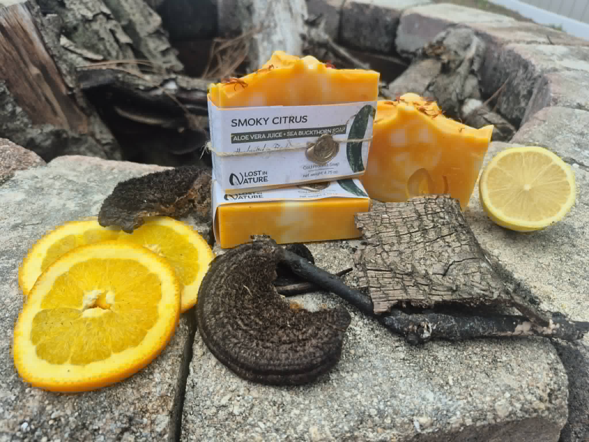 Bright orange Smoky Citrus soap arranged outdoors with citrus and charred wood