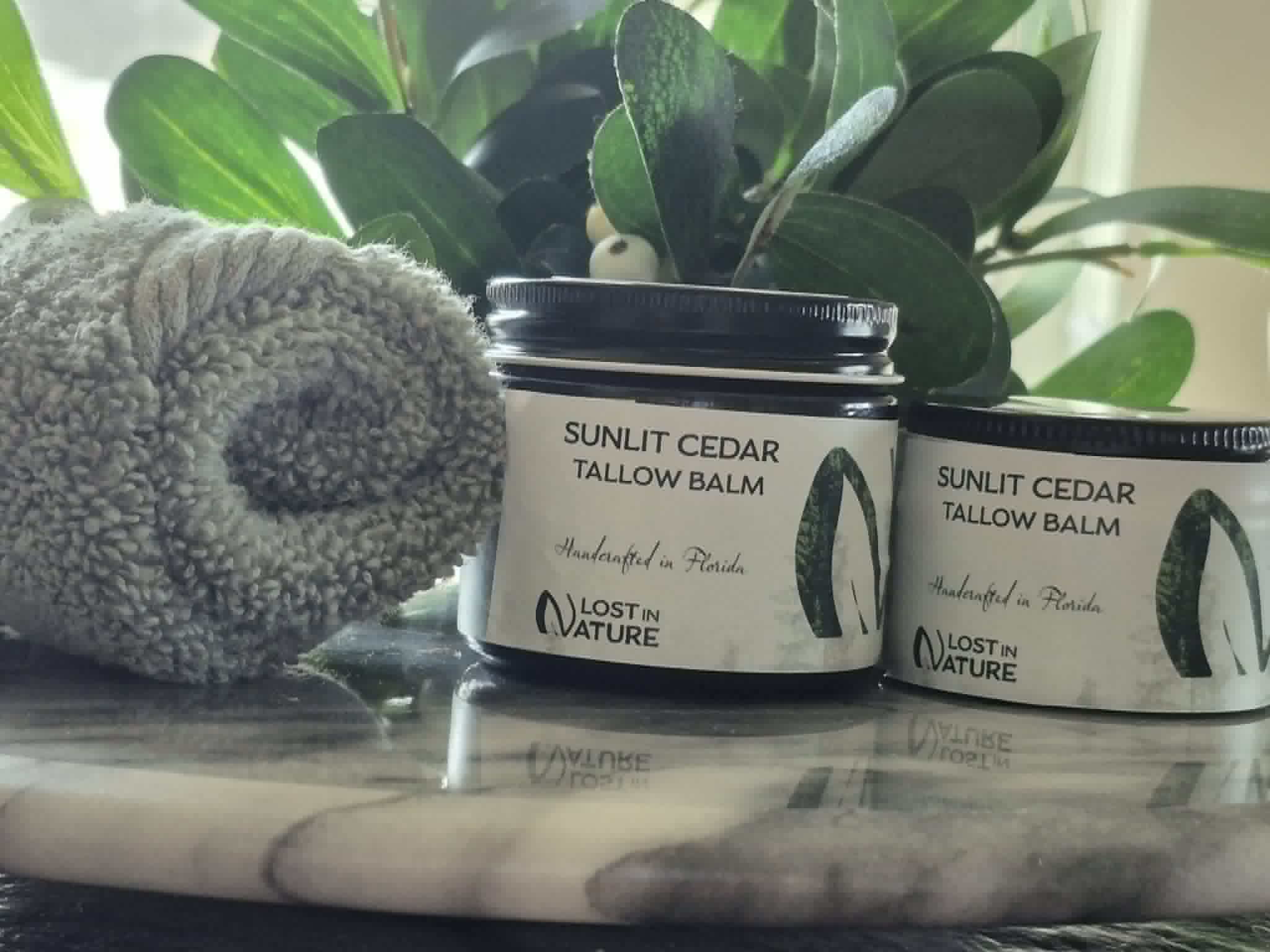 Blue Hill Cedar tallow balm beside a rolled towel and leafy plants